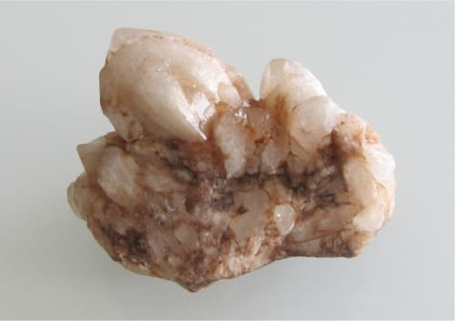A raw quartz crystal cluster, softly lit against a plain ground.