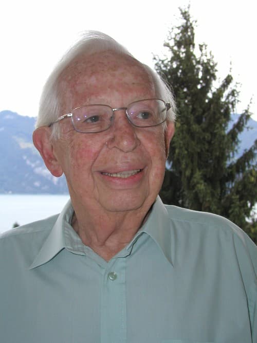 Frank Alper in later life, standing before a lake and mountains, a gentle smile on his face.