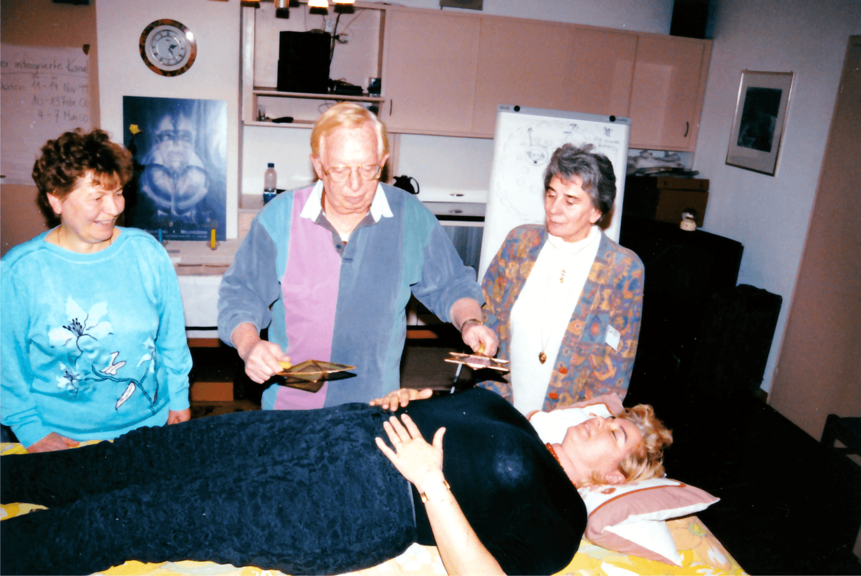 Frank demonstrating an Atlantean Healing Paddle over a person resting on a treatment table, two students looking on.