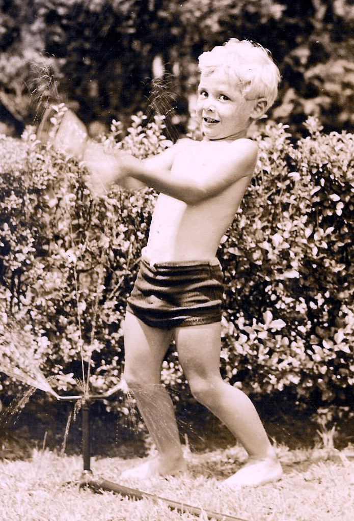 A sepia photograph of Frank Alper as a young boy, playing in a garden.