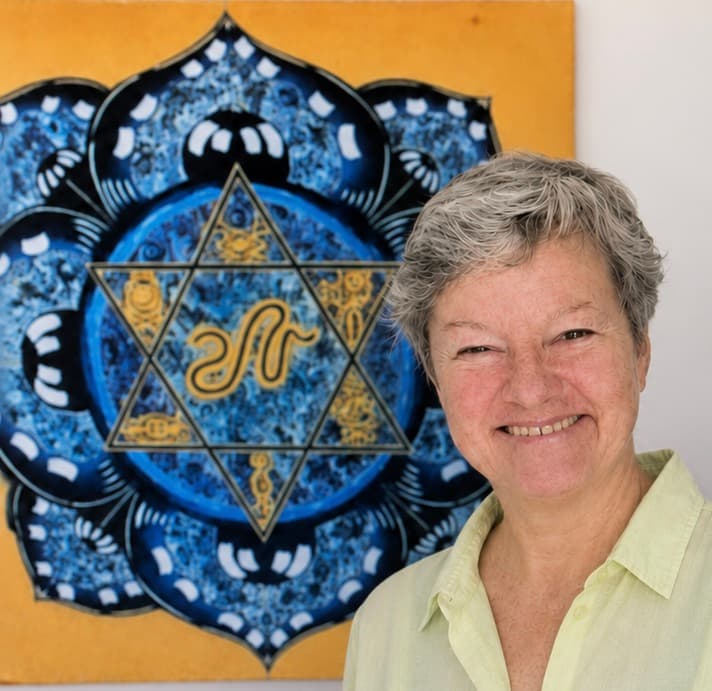 Katharina Alper standing before Frank's Star of Creation — a painted blue lotus mandala with a golden six-pointed star holding a serpent and alchemical symbols at its centre.