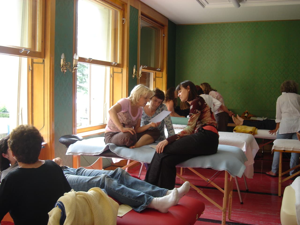 A healing seminar in progress, participants gathered around treatment tables in a light-filled room.
